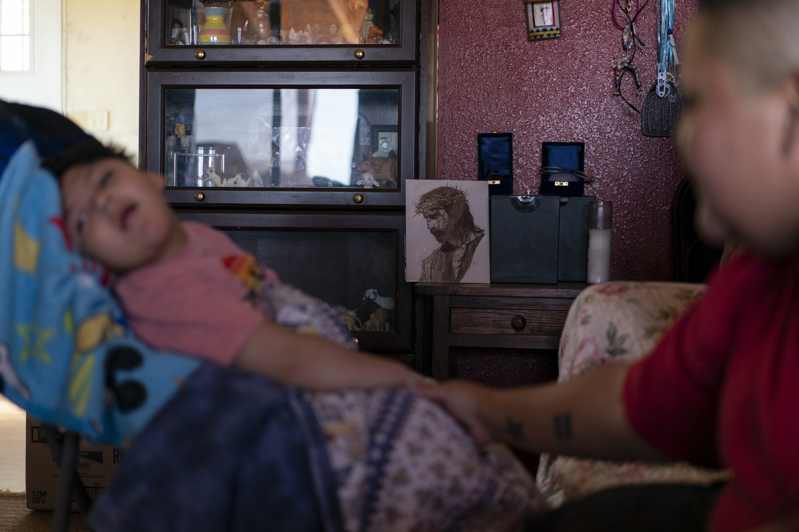 An addult holds the hand of a child with an image of Jesus in the background for a story about Navajo children and the five-year COVID anniversary