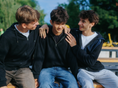 Three teenage boys sit together on a bench.