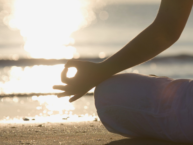 A person sits in meditation on the beach.