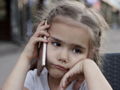 A little girl talks on the phone while frowning.