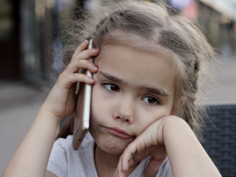 A little girl talks on the phone while frowning.