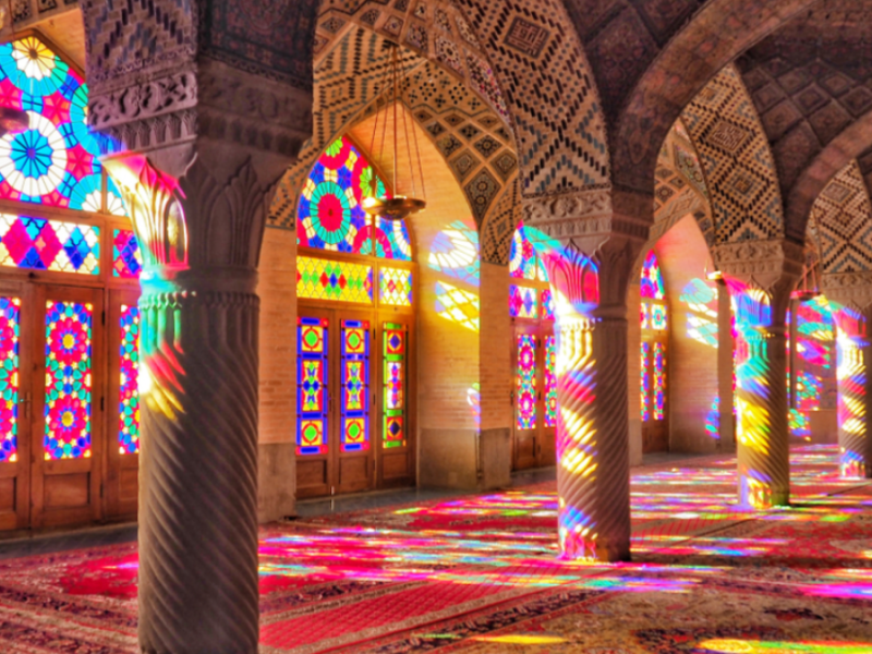 Inside a mosque in Shiraz, Iran, light filters through colorful stained glass windows.
