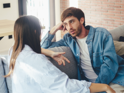 A man and a woman sit on a couch, facing each other, talking