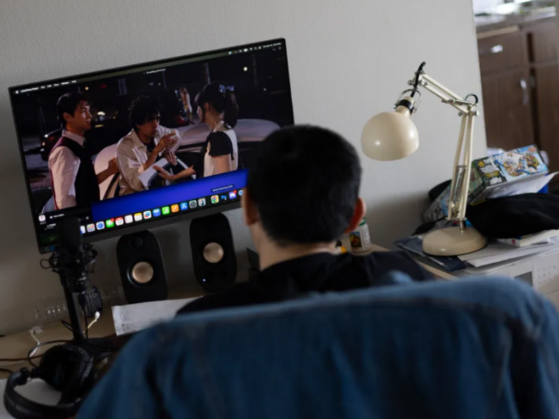 With his back to the camera, a man sits at his desk, watching a scene from a movie on his computer.