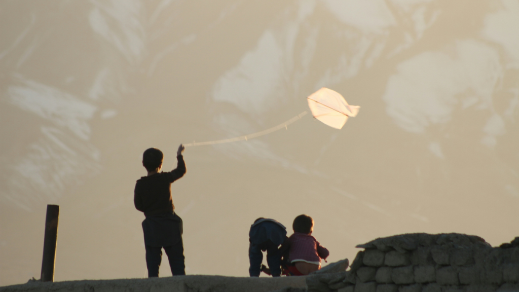 Several young boys are silhouetted against the sky, with one boy holding a string tied to a small kite