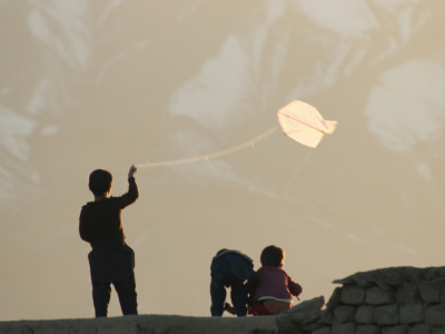 Several young boys are silhouetted against the sky, with one boy holding a string tied to a small kite