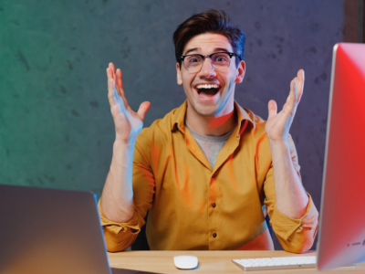 A young man sits at a desk, grinning with excitement.