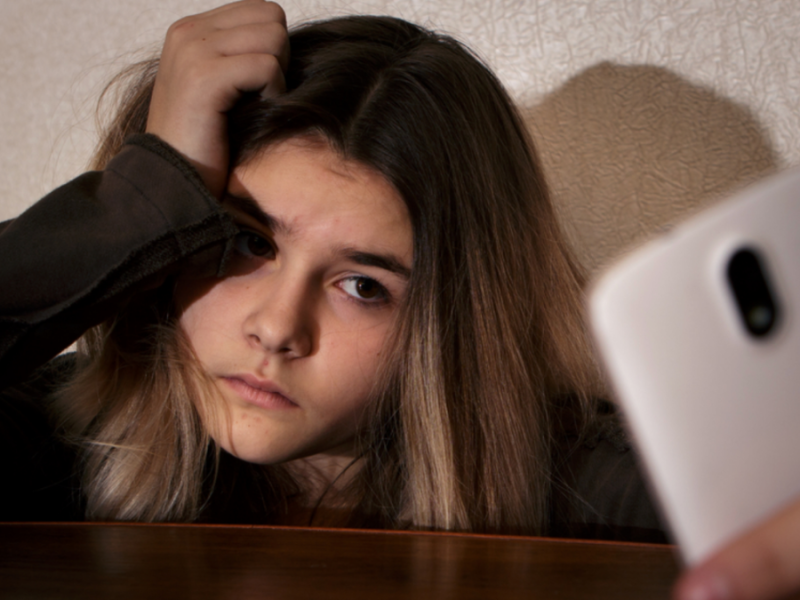 A teenage girl frowns at her phone.