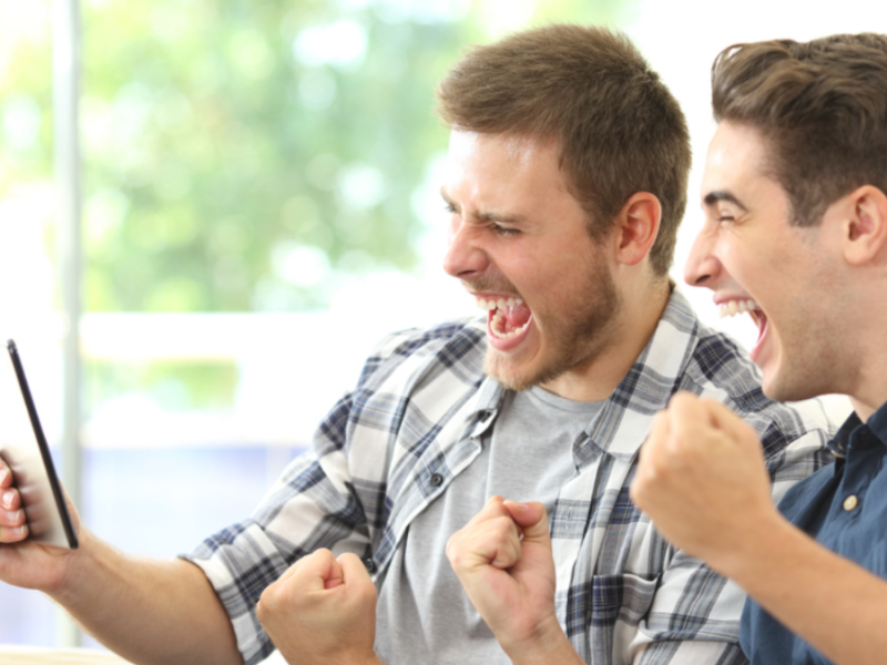 Two young adult men look at a phone, cheering and grinning.