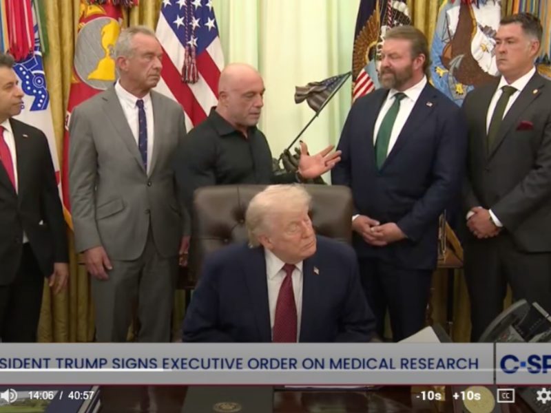 A screenshot of a live feed of President Trump at the bill signing, surrounded by Joe Rogan and several advisors.