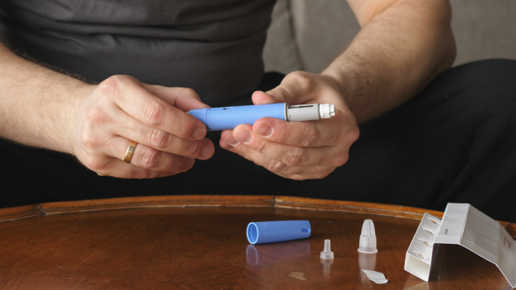 A man sits in front of a table, holding an Ozempic needle in his hands.