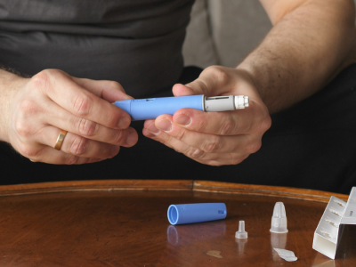 A man sits in front of a table, holding an Ozempic needle in his hands.