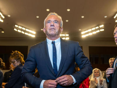 Robert F. Kennedy, Jr. stands in a Senate hearing room, buttoning his jacket.