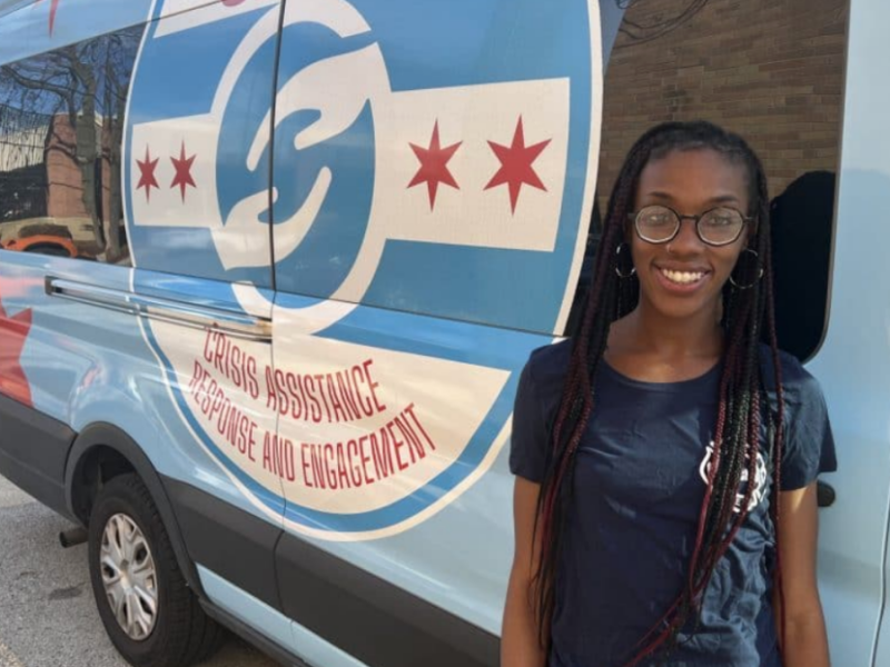 A woman stands in front of a van with a CARE sign on it